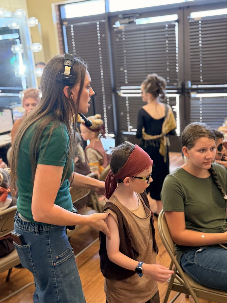 A volunteer on headset guides a Young Artist through the dressing room