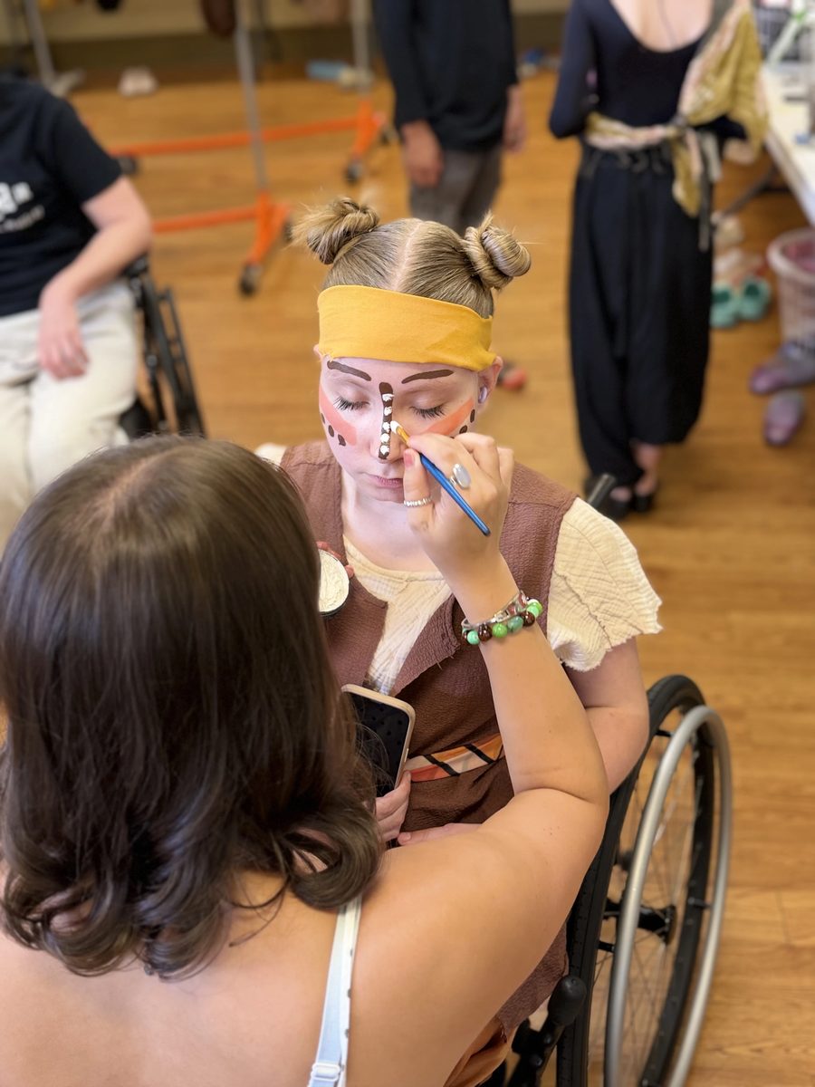 A makeup volunteer adds detail work to a Young Artist’s face